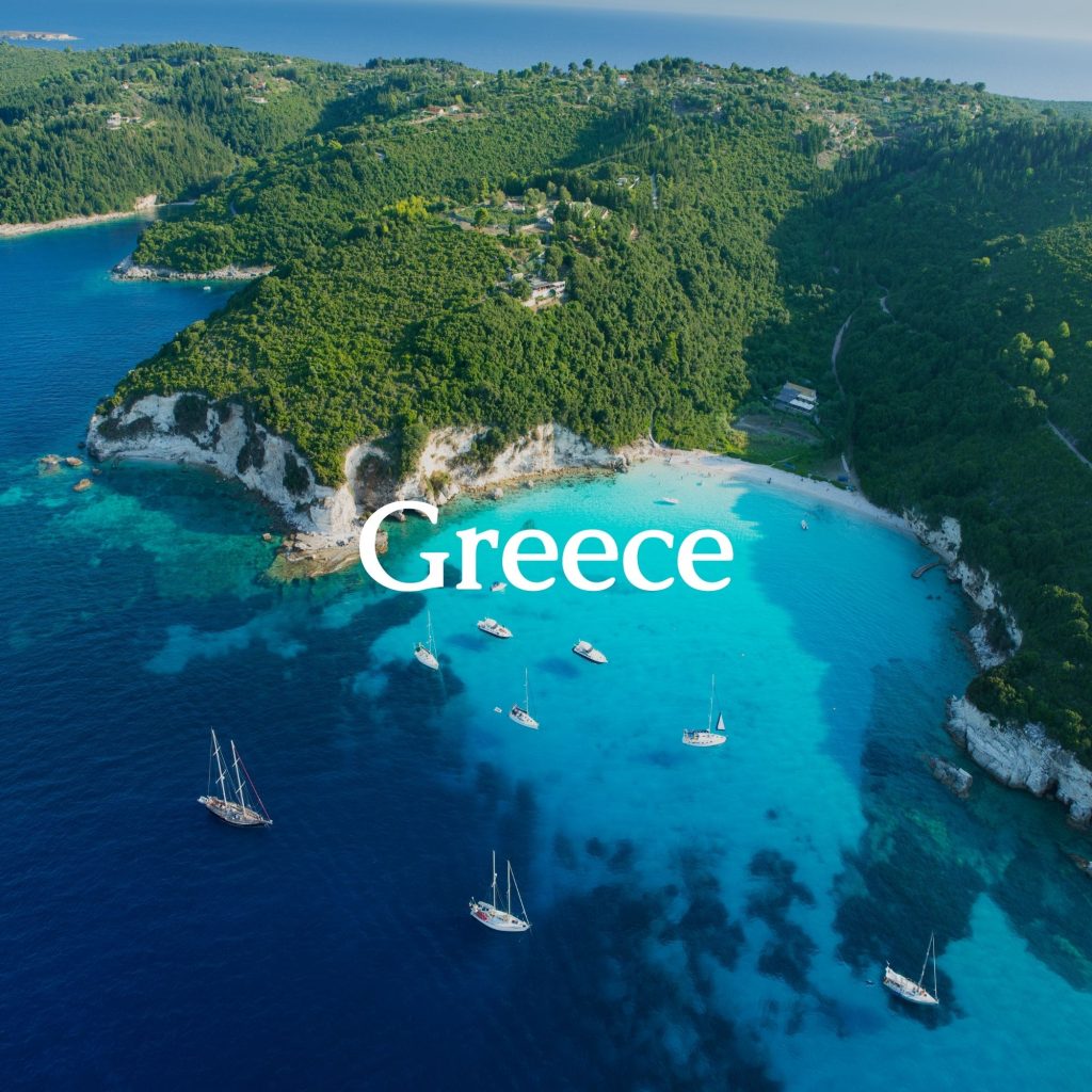 Aerial view of a Greek beach with sailing boats. In the foreground, the sign 'Greece'.